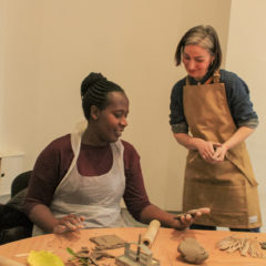 Rebecca May stands in an apron to the side of a workshop participant